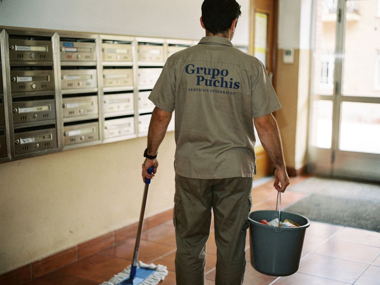 Operario de Grupo Puchis fregando el portal de una comunidad, junto a los buzones